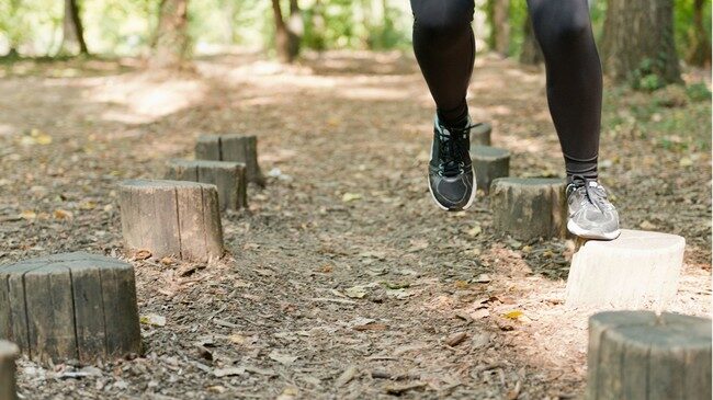 une femme cours dans forêt sur rondins de bois